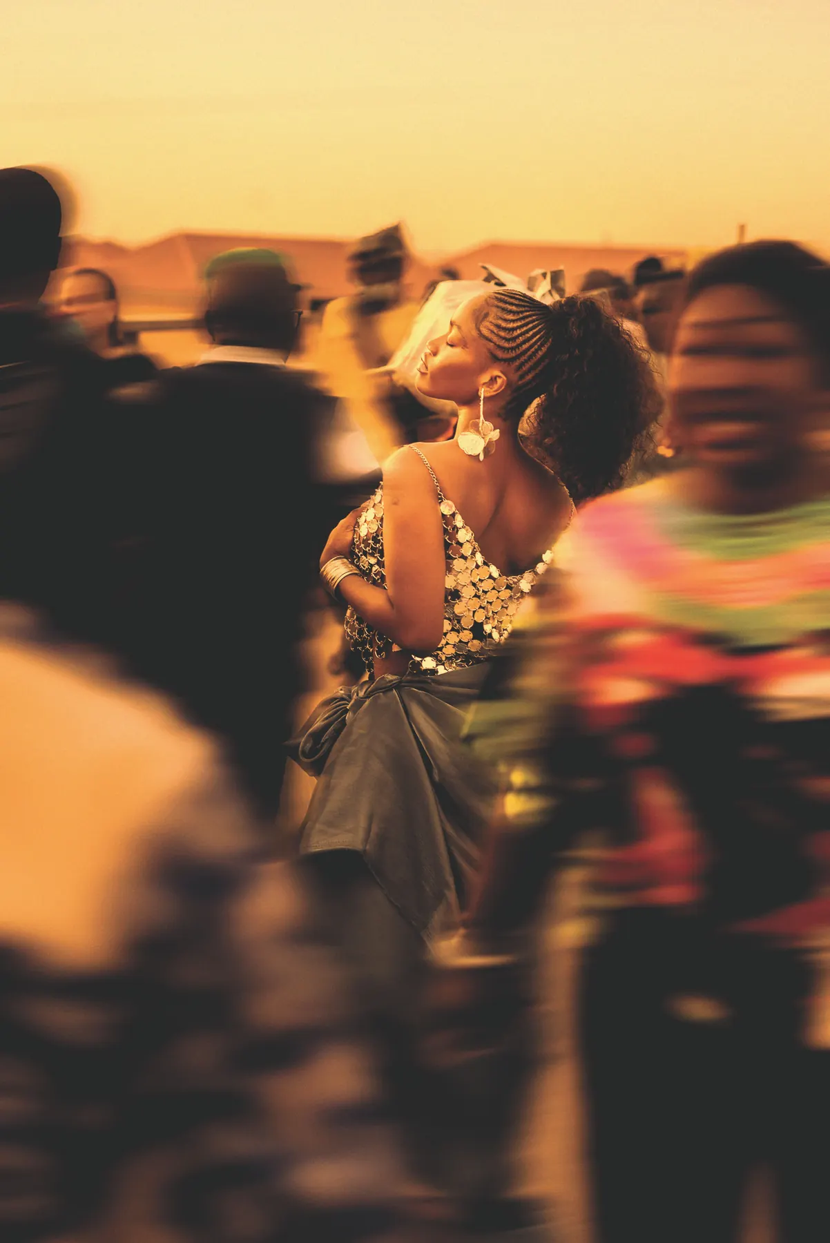 A woman standing still in warm evening light while a crowd moves around her.